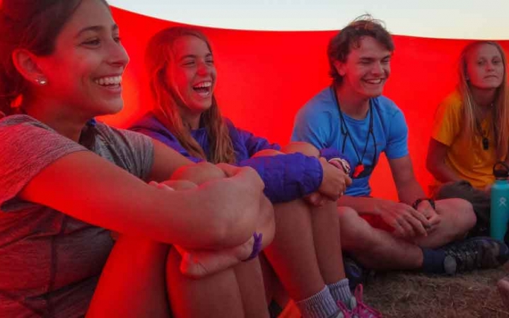 a group of outward bound students laugh while sitting under a tarp on a sea kayaking expedition